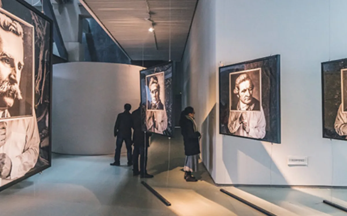 Gallery with large framed black-and-white portraits on white walls, lit from above while visitors look at the work