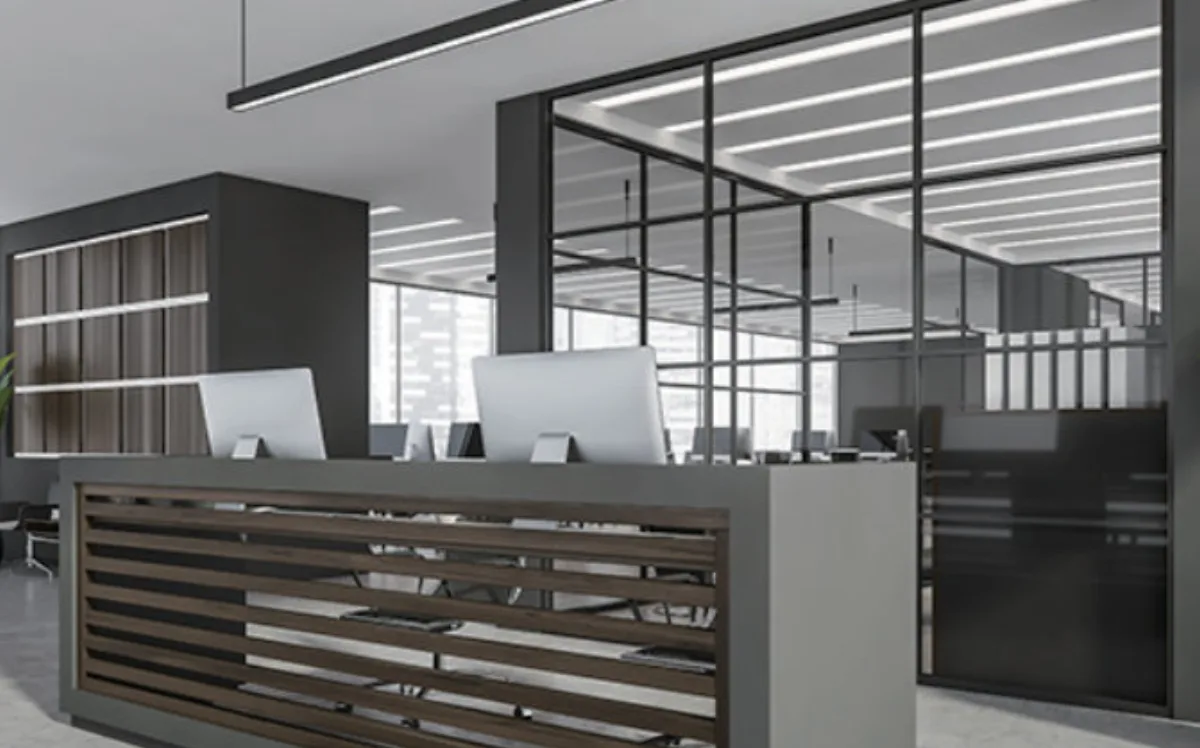Open-plan office with linear lights over the desks, a reception counter and glass-walled meeting rooms